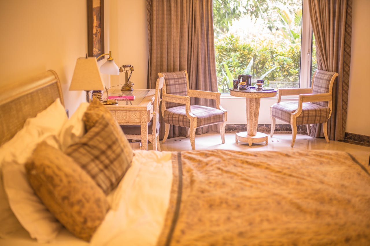 Comfortable sunny hotel room with soft bed and classic armchairs placed near big window aside white vanity table